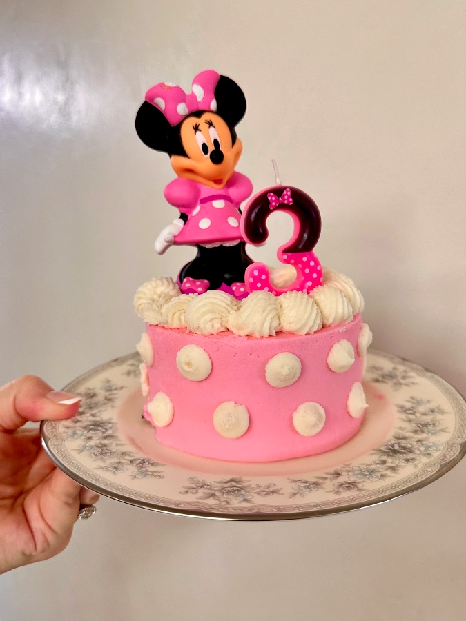 White buttercream cake with a piped pink poodle framed by a rose and vine garland
