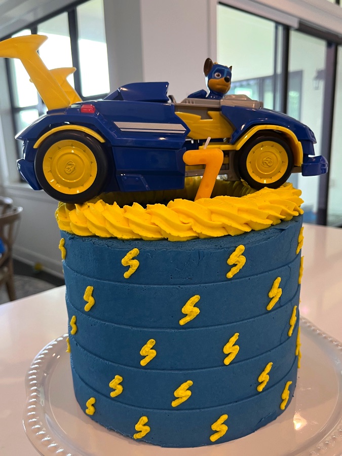 Blue Paw Patrol Chase-themed cake with piped yellow lightning bolts and a number 7 candle