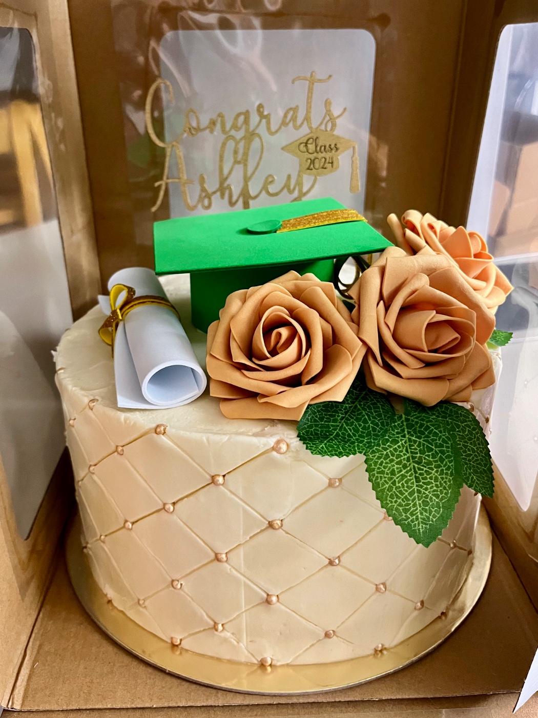 Elegant ivory buttercream cake quilted with pearl dots, topped with cream and peach sugar roses, an edible diploma scroll, and a green graduation cap